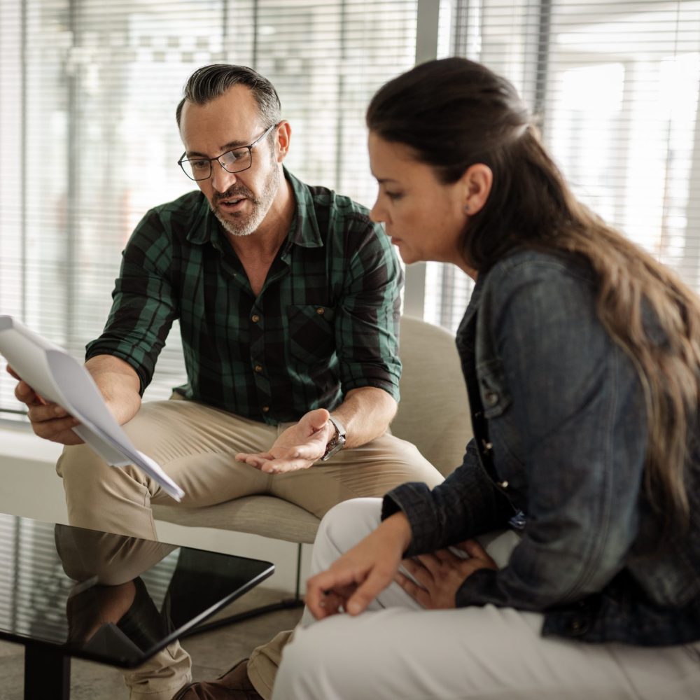 Two mature businesspeople sitting in the lounge area of a modern office and going over paperwork together